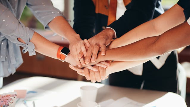 hands from 5 people clasped together in mutual support - like in a physicians anonymous peer support group