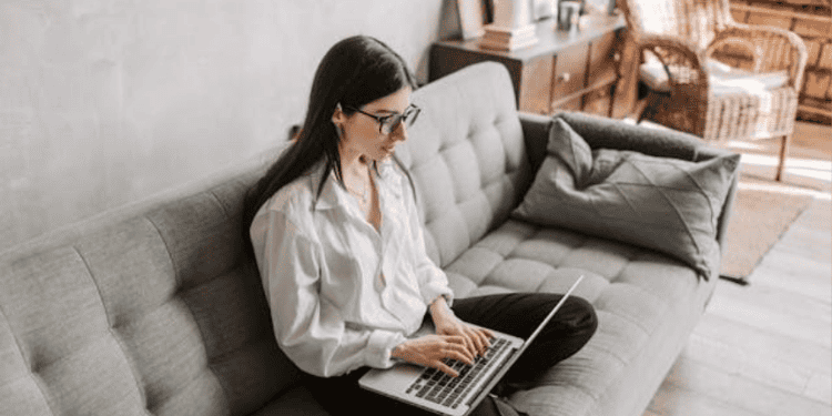 Woman sitting on a couch using a laptop to work online.